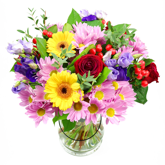This mixed arrangement, displayed in a clear glass vase against a crisp white background, has the generous, welcoming feel of a flower stall suddenly gathered into one abundant bouquet. At the core sit plush red roses, their deep crimson petals layered thickly, conveying sincerity and affection in the way many South Woodford residents choose when sending love or gratitude across the neighbourhood. Flanking them, bold yellow gerbera daisies with dark amber-brown centres beam with a sunny brightness, instantly catching the eye like pockets of light along George Lane on a busy market day. Surrounding these stars of the bouquet, clusters of soft pink and pale lavender daisies or chrysanthemums stretch outward, their small yellow eyes and numerous slender petals forming a halo of softness and gentle colour that adds both volume and tenderness. Tall, graceful stems of lisianthus weave through the design, their purple and lilac bell-shaped blossoms lending depth and an almost satin-like texture that feels quietly refined. Between the petals, polished red hypericum berries appear in small clusters, round and slightly translucent, bringing a lively, contemporary twist amid the more traditional blooms. Layers of fresh greenery, from broad, glossy leaves to finer, feathery sprigs, cradle the flowers, creating a natural framework that suggests a hand-gathered, garden-fresh style often requested for local celebrations near Eagle Pond and surrounding streets. The clear vase showcases the neatly aligned stems and pristine water, underlining the care taken in conditioning each flower. Overall, the bouquet gives off a sense of warm celebration and thoughtful artistry, suited for birthdays, congratulations, or simply brightening a South Woodford living room with a burst of colour and life.