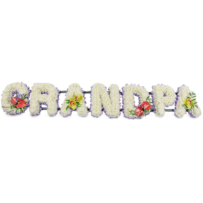A dignified funeral tribute in the shape of the word GRANDPA stretches horizontally across the frame, every letter composed with the meticulous care of an experienced South Woodford florist. Each capital letter is filled edge to edge with small, crisp white chrysanthemums, packed so closely that their layered petals form a dense, cushiony surface, almost like freshly fallen snow. The cool white flowers capture the soft light and give the arrangement a calm, contemplative presence. Framing the base of each letter is a subtle trim of pale lavender ribbon, a fine band of colour that traces the contours and brings gentle definition without overpowering the simplicity of the design. The letters sit securely on dark green bars, hidden as much as possible but ensuring the tribute can be displayed confidently at a funeral service or wake. Carefully placed sprays of accent flowers bring moments of rich colour and storytelling to the piece. On the left-hand 'G', a striking group of deep red anthuriums, with their glossy, heart-shaped spathes and central yellow spadices, rests among lush green foliage and tiny hints of purple filler blooms, suggesting passion, respect, and enduring love. The first 'A' is softened with yellow-green orchids, their delicate petals and curved stems arranged with verdant leaves to introduce a note of elegance and remembrance. The central 'D' repeats the red anthurium cluster, creating balance across the word, and the final 'A' mirrors the orchid spray, giving a sense of harmony from start to finish. This GRANDPA tribute is the kind of bespoke design chosen for funerals and celebrations of life around South Woodford, offering a tangible expression of gratitude, affection, and farewell to a cherished grandfather.