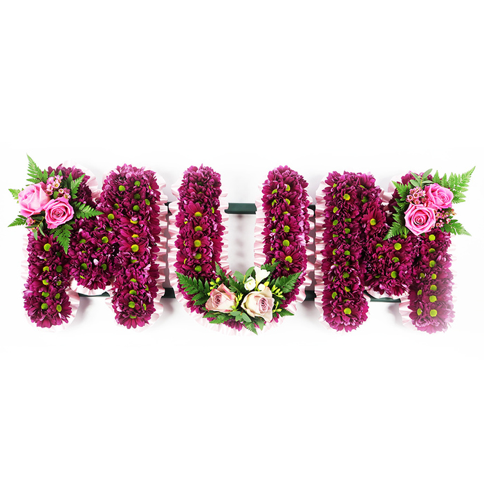 A beautifully balanced floral arrangement spells out MUM in large, three-dimensional letters that appear to hover gently against a spotless white background, making every petal and ribbon detail clearly visible. The faces of the letters are completely filled with compact sprays of vivid magenta and deep purple chrysanthemums, their numerous petals creating a plush, tapestry-like effect. At the heart of each tiny bloom, a lime-green centre glows softly, adding depth and a subtle brightness that keeps the design from feeling heavy. These chrysanthemums are placed so tightly that no gaps are visible, giving the letters a sculpted, almost cushioned appearance that feels both formal and warmly inviting. Tracing the outline of each letter, a delicate pale pink ruffled ribbon has been carefully pleated and attached, its softly frilled edges adding movement and a gentle, fabric-like softness to the strong floral forms. On the upper left side of the first M, an accent spray of bright pink roses and rosebuds rests among airy green fern fronds and small leaves, echoing the natural charm of parks and gardens around South Woodford. The central U features a graceful embellishment at its base, where blush pink and cream roses are arranged with variegated greenery and tiny white flowers, forming a quiet, soothing crescent. The top right of the final M carries a complementary cluster of vibrant pink roses and fresh fern foliage, creating a visual conversation from one side of the tribute to the other. Crafted with the kind of precision and care you would expect from an experienced local florist, this MUM tribute is a tender choice for funerals, wakes, or graveside farewells throughout South Woodford, symbolising devotion, remembrance, and unspoken gratitude.