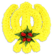 A large, vibrant floral tribute carefully sculpted into the Khanda - the sacred Sikh emblem - sits photographed against a plain white backdrop, its bright colours and textures described as clearly as I would to a customer at my South Woodford bench. The entire symbol - the circular chakkar, the central double-edged khanda sword and the two crossed kirpans beneath - is rendered from countless small, tightly packed yellow chrysanthemums that form a plush, slightly three-dimensional surface. The yellow blooms are arranged so their ruffled petals catch soft studio light and seem to ripple outward along the emblem's sweeping curves, giving the piece a warm, golden glow that reads both respectful and hopeful. At the point where the chakkar meets the khanda, a tight cluster of deep red roses - five or six classic buds - creates a commanding focal point; their velvety petals are cradled by a collar of dark green fern fronds, the glossy, serrated leaves providing a cool, structured contrast to the sunlit yellow. A faint, clean floral scent is implied by the composition, a subtle mix of sweet rose and fresh greenery. The white background and the soft grey shadow under the arrangement emphasize that this is a substantial, solid tribute, likely intended for a funeral, memorial, or religious ceremony honoring Sikh heritage. As a florist familiar with the South Woodford community - from George Lane to the area around the tube station - I'd present this piece with quiet care for families seeking a dignified, symbolically faithful floral offering.