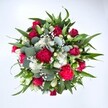 Viewed from directly above against a pristine white background, this luxurious bouquet feels like a vibrant celebration captured in a single moment. At its centre, deep crimson red roses cluster together, some still tightly furled, others just beginning to unfurl their velvety petals, creating a heart of classic romance. Around them, rich fuchsia and ruby red carnations form a ruffled halo, their densely layered petals adding movement and a sense of joyful exuberance. Nestled between the bolder blooms are clusters of small, daisy-like white spray chrysanthemums, each neat flower head offering a clean, bright contrast that lifts the entire arrangement. Tiny white gypsophila - baby's breath - drifts delicately through the bouquet, like a fine mist of stars softening the edges and filling any gaps with gentle lightness. Lush green foliage frames the flowers: broad, pointed dark green leaves give structure and depth, while rounded, silvery eucalyptus leaves weave through the design, introducing cool blue-green tones and a contemporary elegance. The bouquet is tightly composed, creating a full, rounded shape that feels generous and carefully crafted, as though it has just been finished on a busy workbench in a South Woodford flower shop. The lighting is clear and even, highlighting the rich reds, crisp whites, and varied greens without casting harsh shadows. This is the kind of arrangement that might arrive for a birthday on George Lane, an anniversary surprise near Eagle Pond, or as an uplifting get well soon delivered to a home off Hermon Hill - a spirited, joyful gift that speaks of affection, vitality, and heartfelt thoughtfulness through colour, texture, and impeccable floristry.